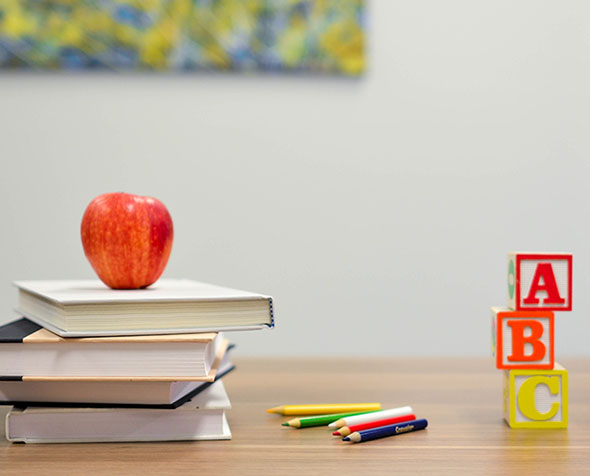 apple on stack of books next to colored pencils and a b c blocks on desk