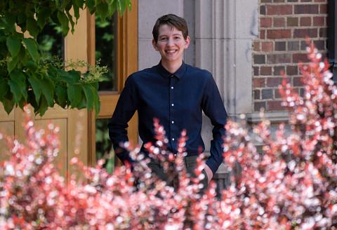 Flynn stands in front of a DU building with spring flowers in the foreground.